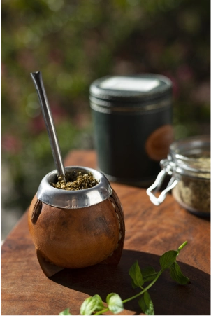 Traditional leather-bound mate gourd with a metal bombilla straw filled with yerba mate leaves on a wooden table.